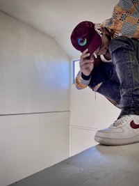a man crouching on a ledge while wearing a hat and sneakers