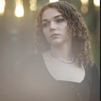 a woman with curly hair standing in the woods