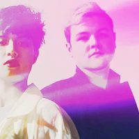 two people standing next to each other in front of a purple light