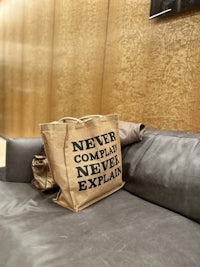 a bag with the words never complacent never explain sitting on top of a leather couch