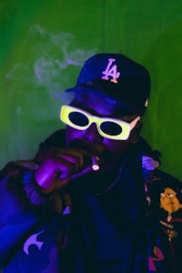 a man wearing sunglasses and a cap smoking a cigarette