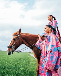 two women standing on a horse in a field
