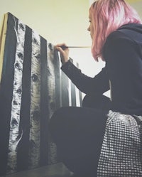 a woman with pink hair painting birch trees on canvas