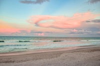 a beach with a pink sky and clouds in the background