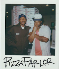 two men posing in front of a pizza parlor