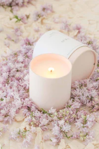 a white candle surrounded by lilac flowers