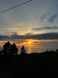 the sun is setting over a lake with trees in the background