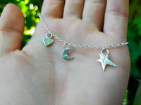 a hand holding a silver bracelet with a star, moon and heart