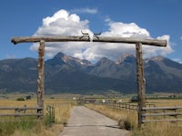 a wooden gate leading to a dirt road with mountains in the background