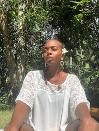 a woman in a white shirt sitting on a bench in the woods