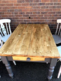 a wooden table with white chairs in front of a brick wall