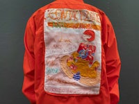 a man wearing an orange jacket with embroidered designs on it