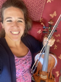 a woman smiling while holding a violin on a couch