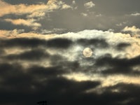 the moon is seen through a cloudy sky
