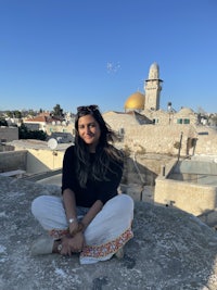 a woman sitting on top of a wall in front of the dome of the rock