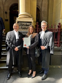 three people standing in front of a building holding a certificate