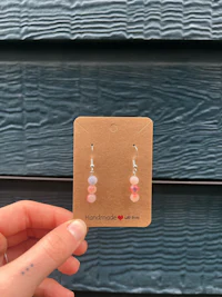 a person holding up a card with a pink stone dangling from it