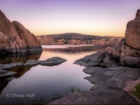 a lake surrounded by rocks and boulders at sunset