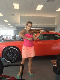 a woman playing a violin in front of a car