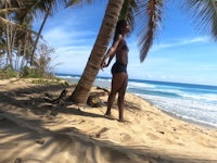 a woman standing on the sand next to a palm tree
