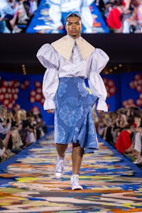 a model walks down a runway wearing a blue shirt and blue skirt