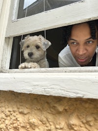 a woman peering out of a window with a white dog