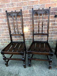 a pair of carved wooden chairs in front of a brick wall