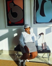 a woman wearing a hat and skirt sitting in front of a painting