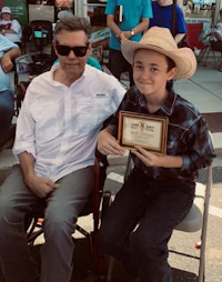 a man in a cowboy hat and a boy in a wheelchair holding a plaque