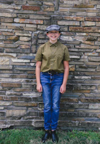 a girl in jeans and a hat standing in front of a stone wall