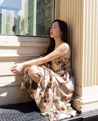 a woman sitting on the steps of a building in a floral dress