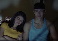 a man and woman sitting on a bed in the dark