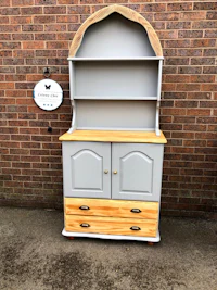 a grey and wooden hutch with drawers in front of a brick wall