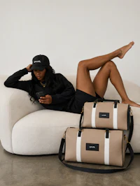 a woman sitting on a couch with two duffel bags