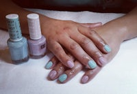 a woman's hand with blue and green nails and a bottle of nail polish