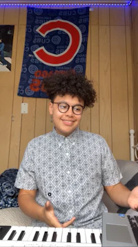 a young man with glasses is playing a keyboard in his room