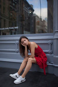 a woman in a red dress leaning against a wall