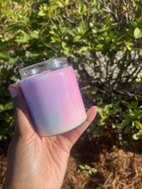 a person holding a pink and purple candle in front of bushes
