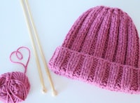 a pink knitted hat with knitting needles and yarn