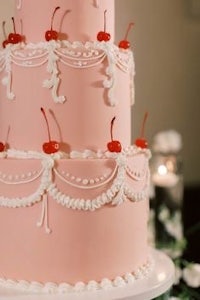 a pink wedding cake with cherries on top
