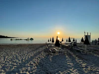 the sun is setting over a beach with chairs and umbrellas