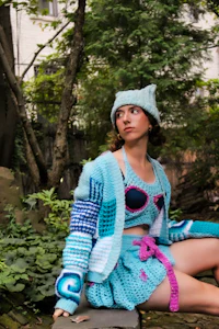 a woman in a blue knitted outfit sitting on a rock