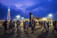 a crowd of people standing in a dirt field at dusk