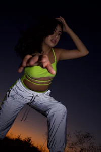 a woman in a neon top and white pants is posing at night