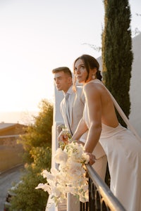 a bride and groom standing on a balcony at sunset