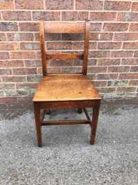 a small wooden chair against a brick wall