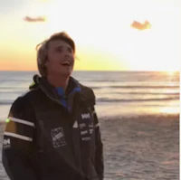 a man in a jacket standing on the beach at sunset