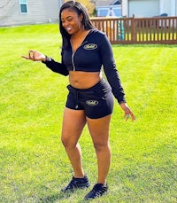 a woman in black shorts and a hoodie standing in a grassy area