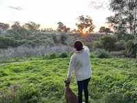 a woman is walking her dog in a field at sunset