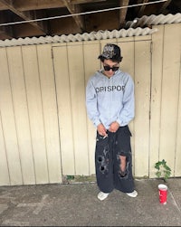 a man wearing a hoodie standing next to a wall